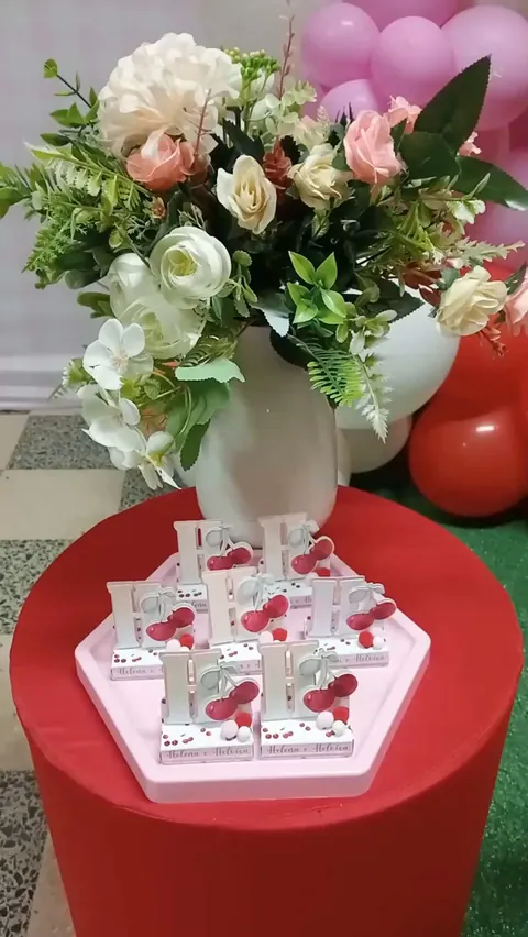 Arranjo de flores brancas e rosas sobre mesa vermelha numa festa com tema cerejinhas